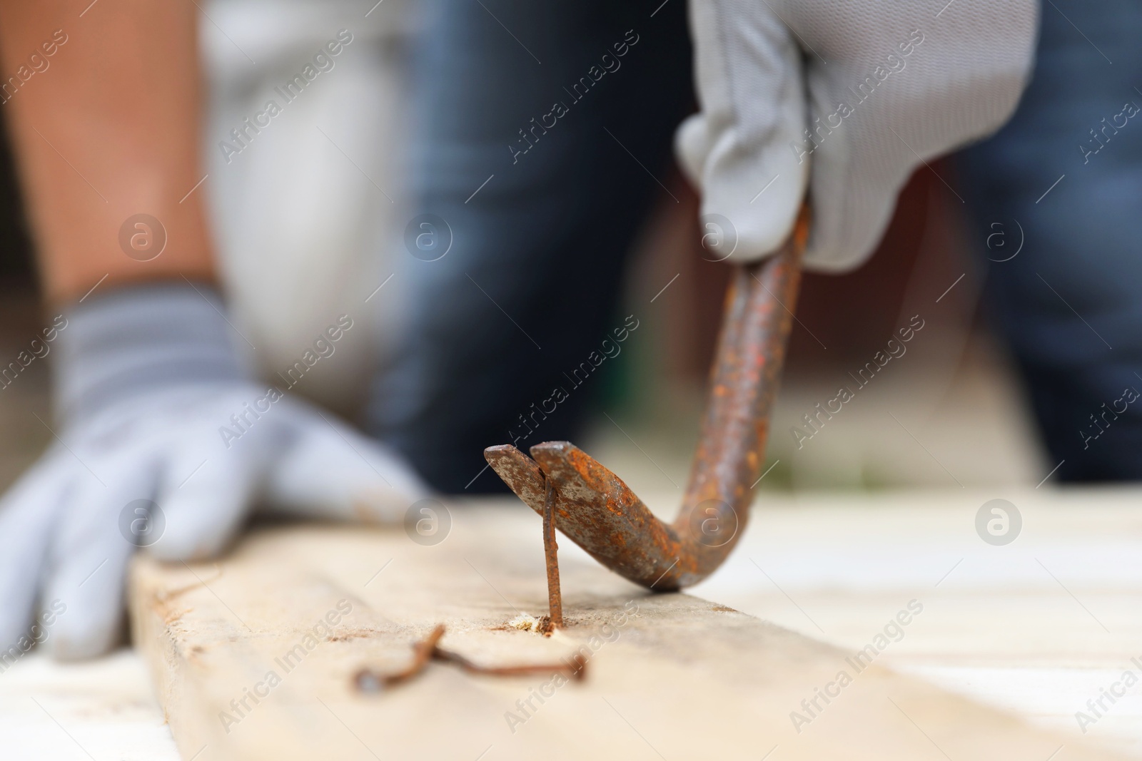 Photo of Man pulling metal nail out of wooden plank with crowbar outdoors, closeup