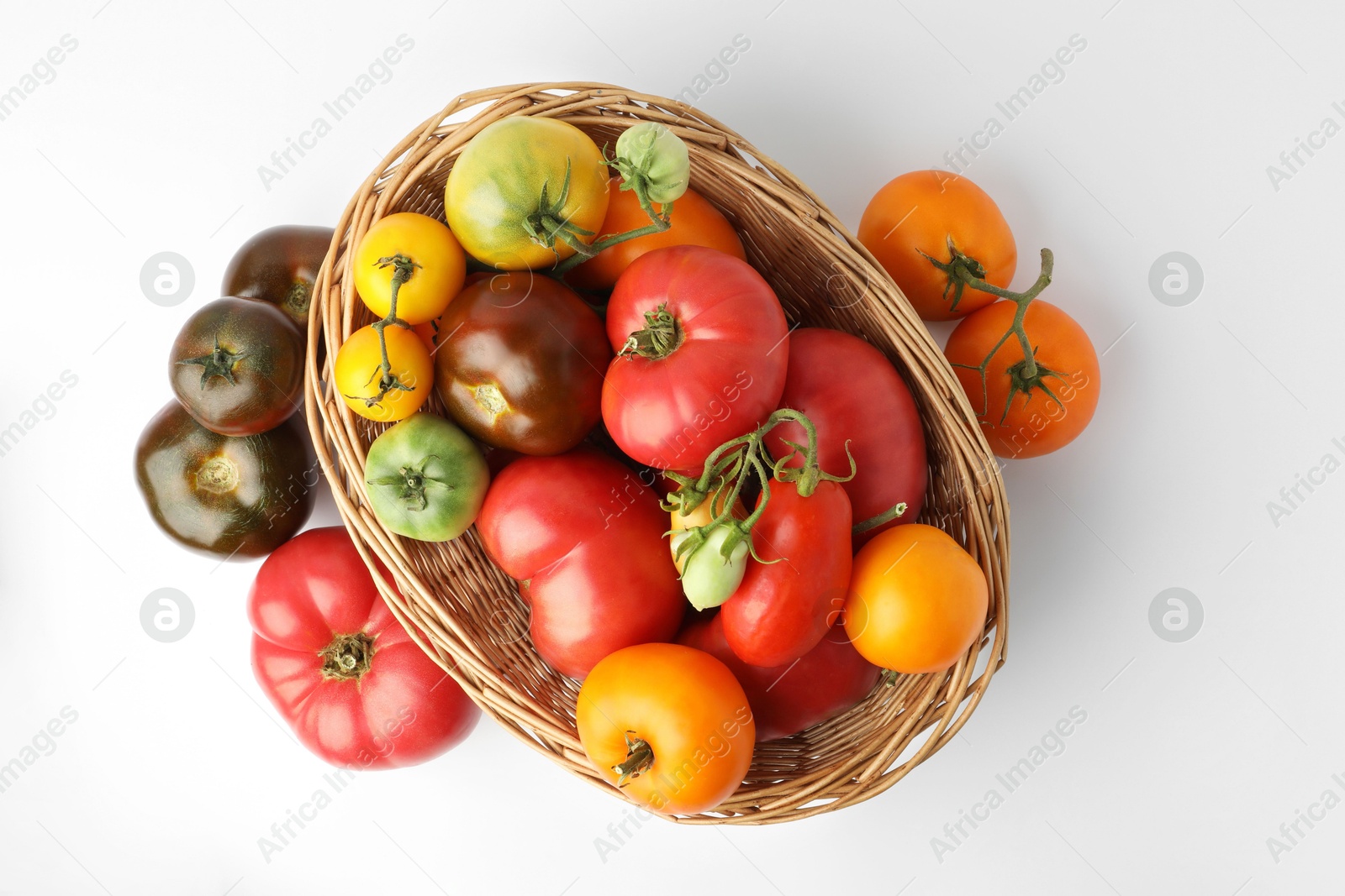 Photo of Different ripe tomatoes in basket on white background, top view