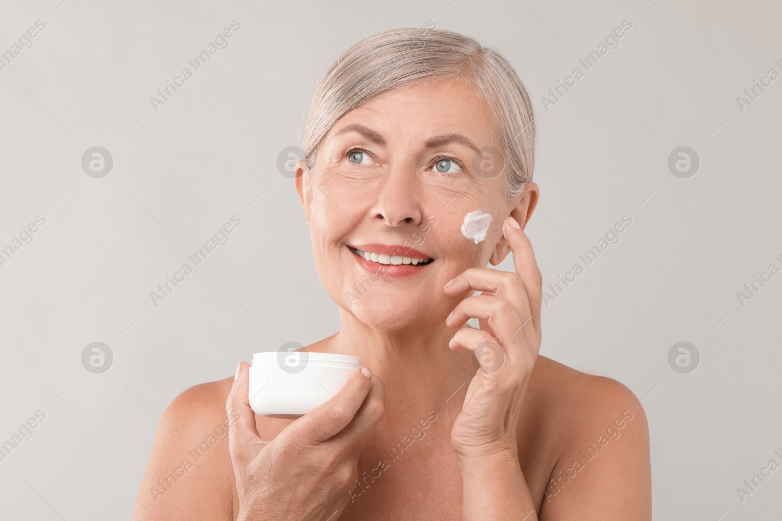 Photo of Senior woman applying face cream on light background