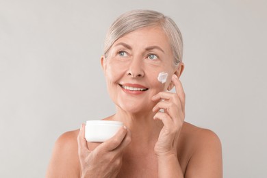 Senior woman applying face cream on light background