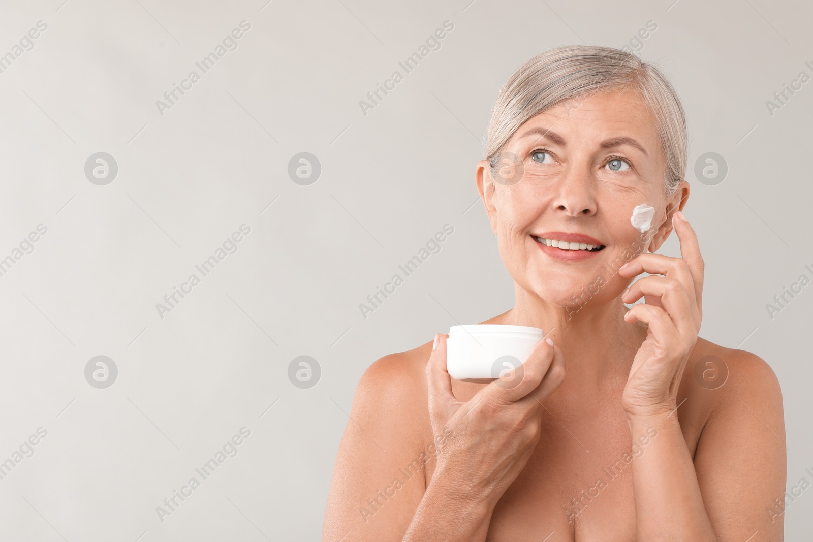 Photo of Senior woman applying face cream on light background. Space for text