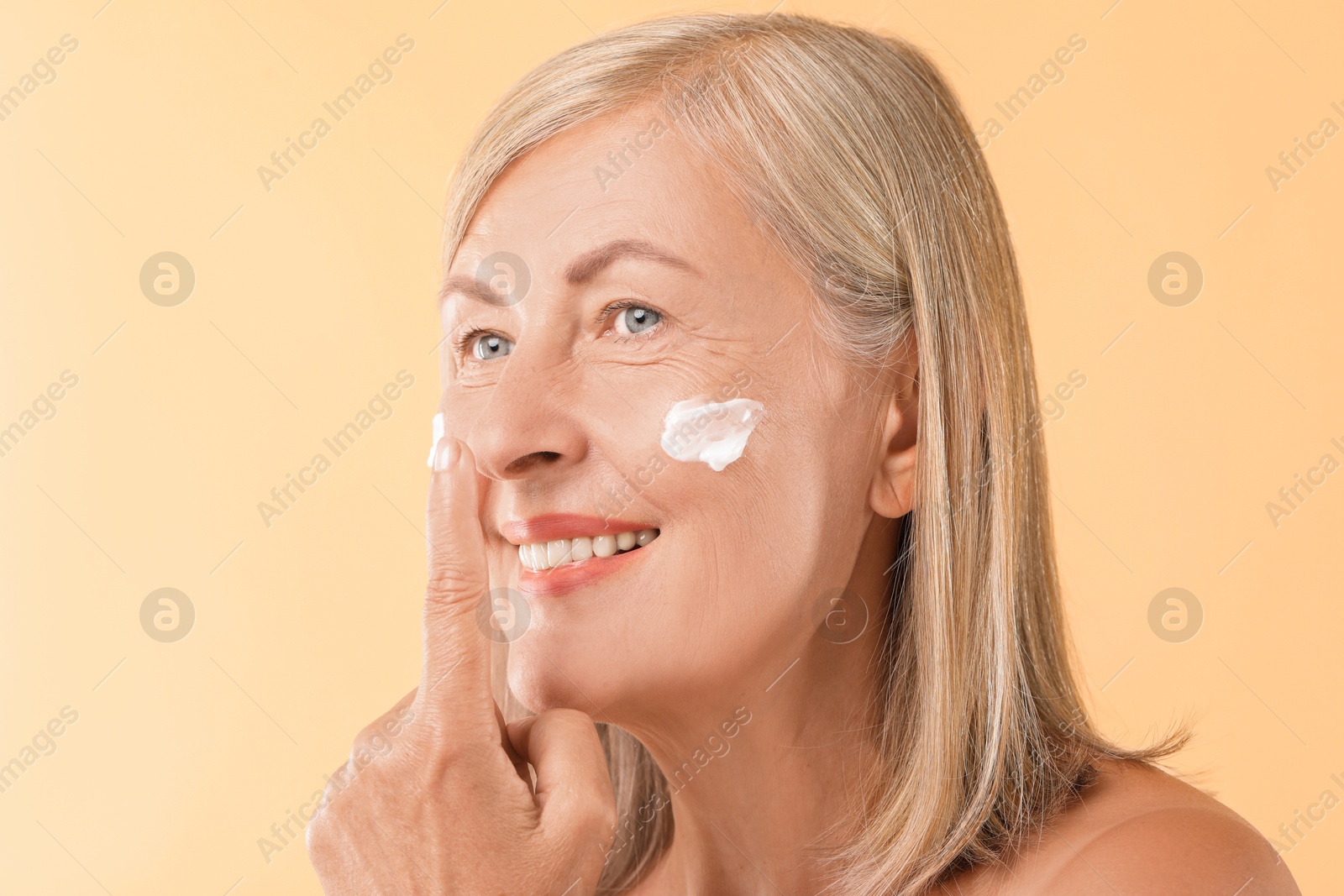 Photo of Senior woman with face cream on beige background