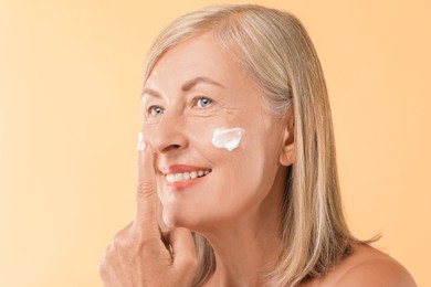 Senior woman with face cream on beige background