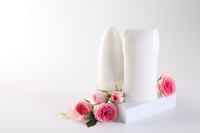 Photo of Different deodorants beautiful rose flowers on white background, space for text