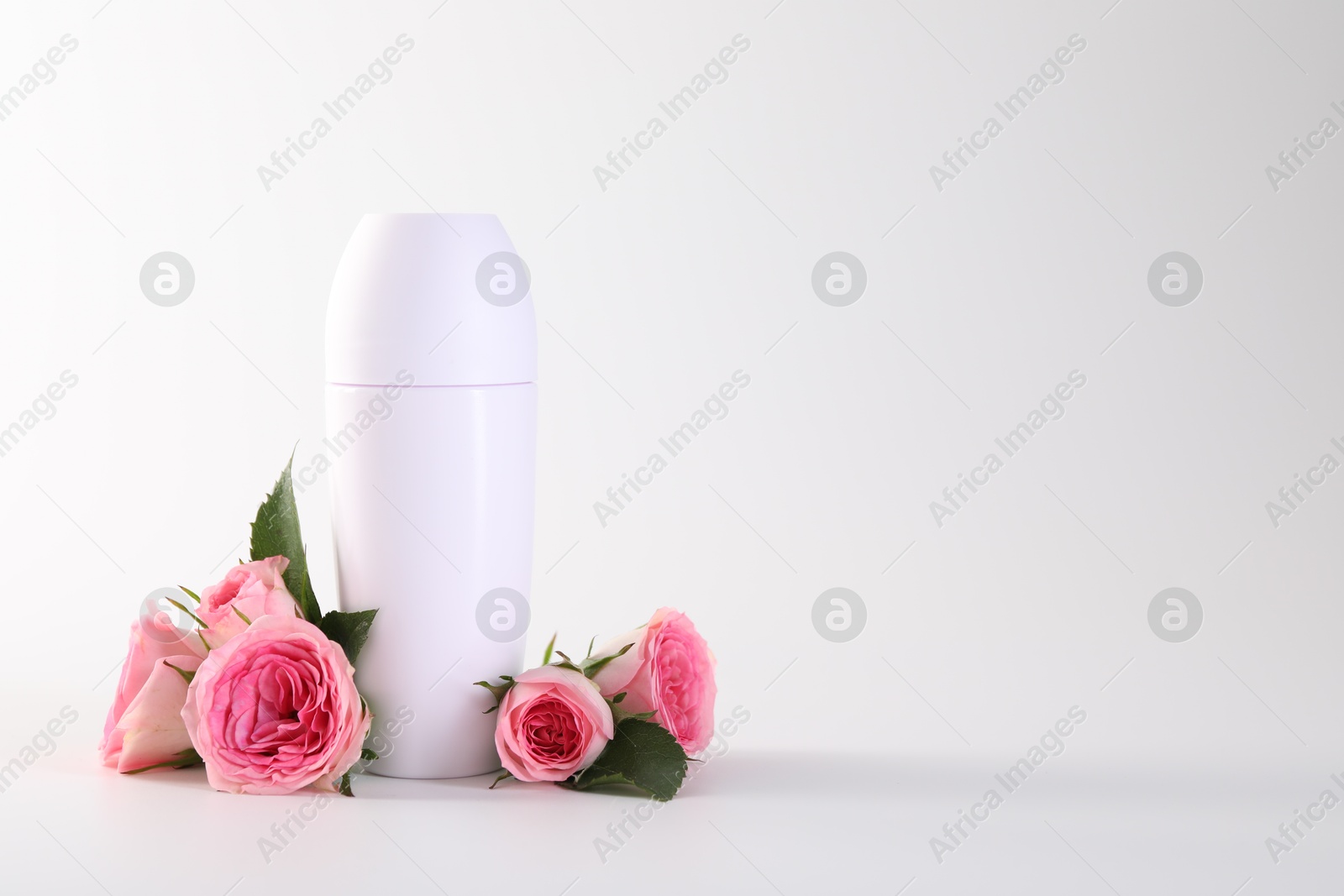 Photo of Roll-on deodorant and beautiful rose flowers on white background, space for text