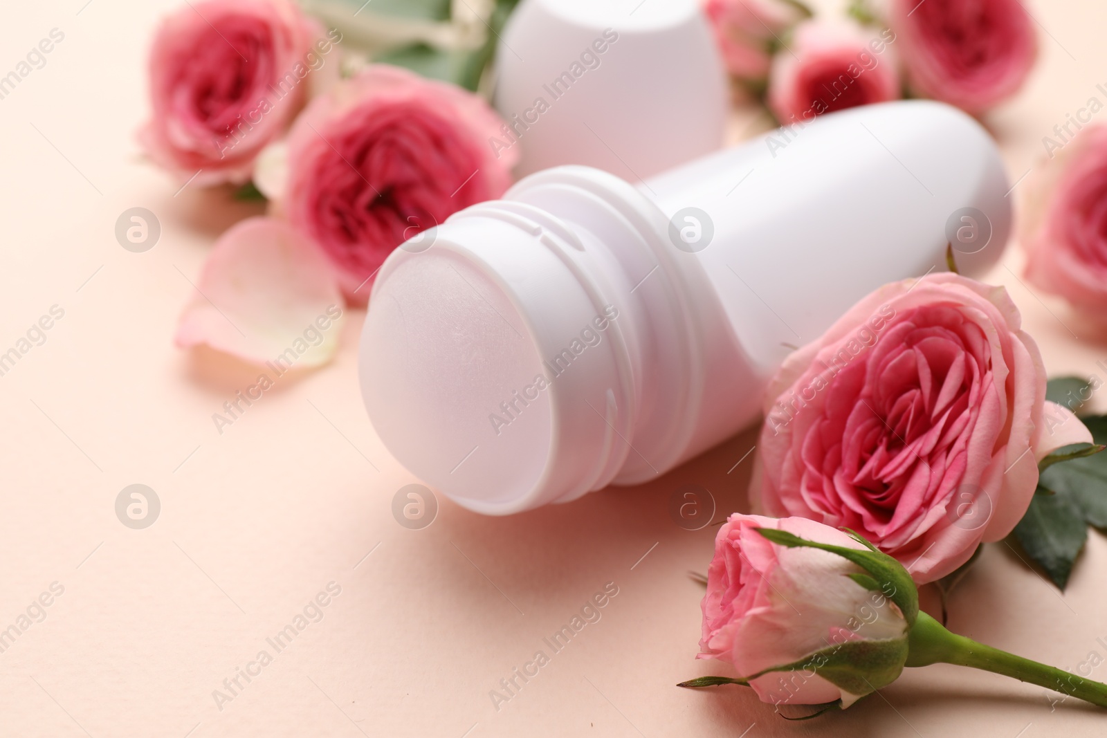 Photo of Roll-on deodorant and beautiful rose flowers on beige background, closeup