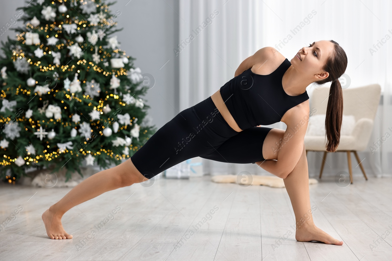 Photo of Woman practicing yoga against Christmas tree indoors