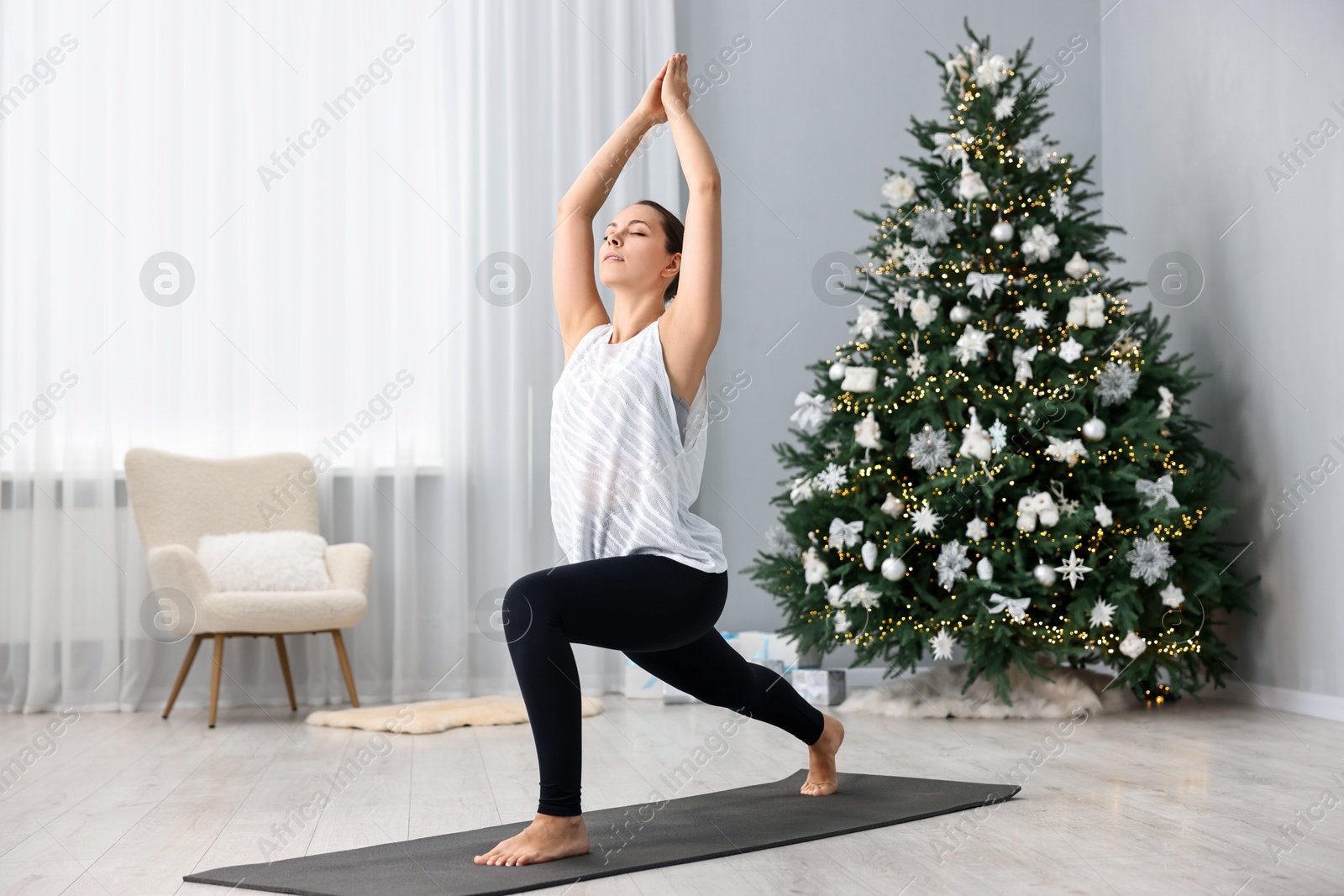 Photo of Woman practicing yoga against Christmas tree indoors