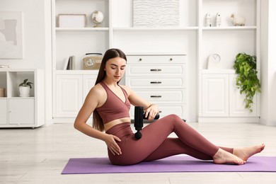 Woman using percussive massager to relieve hip muscles on mat at home