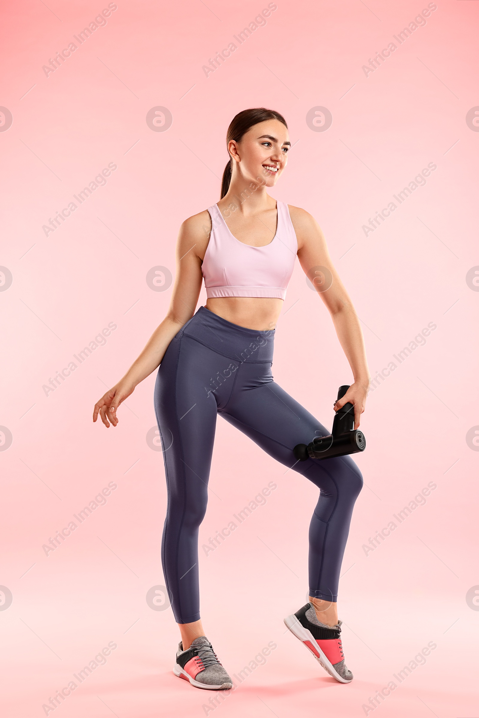 Photo of Woman using percussive massager to relax thigh muscles on pink background