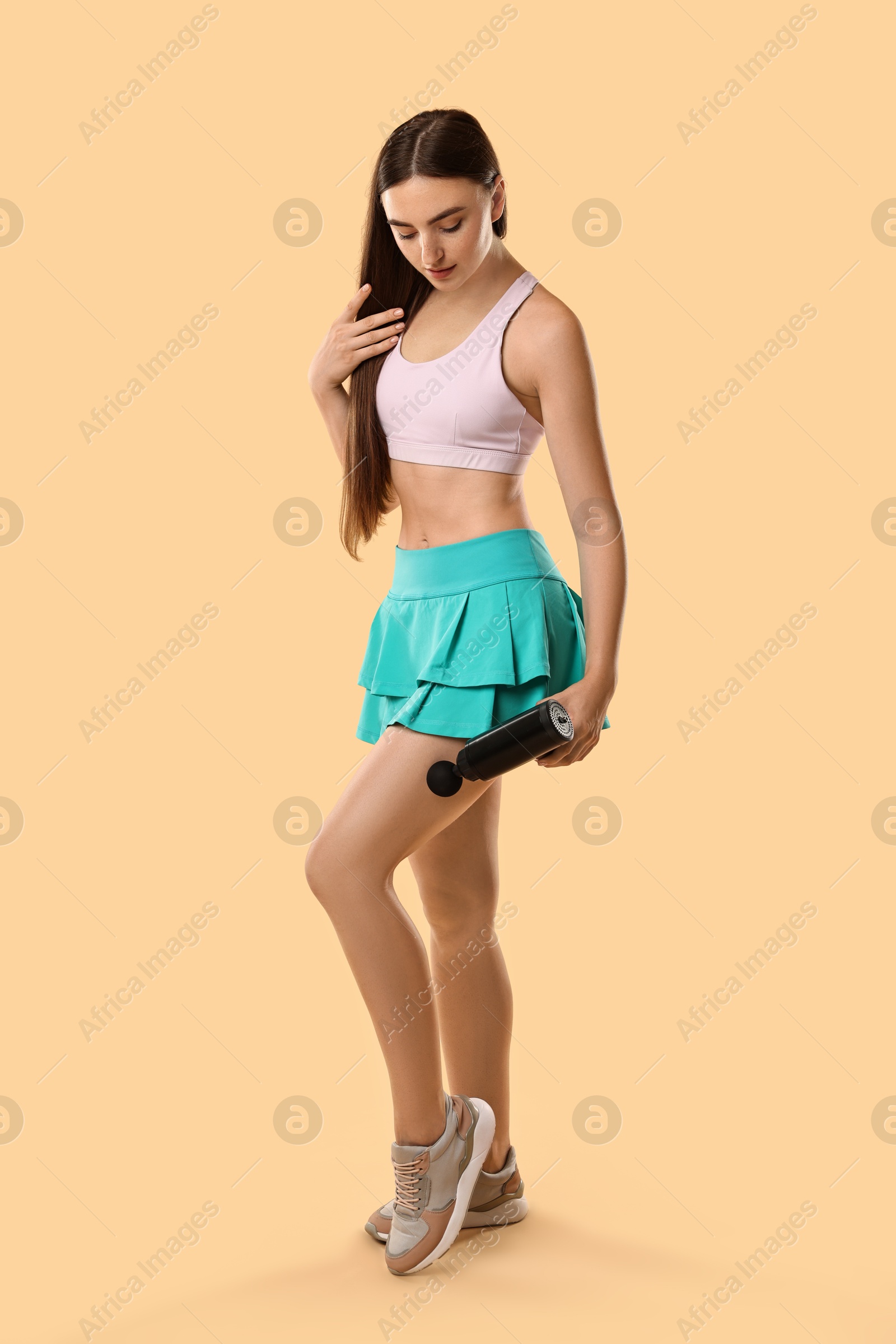 Photo of Woman using percussive massager to relax thigh muscles on beige background