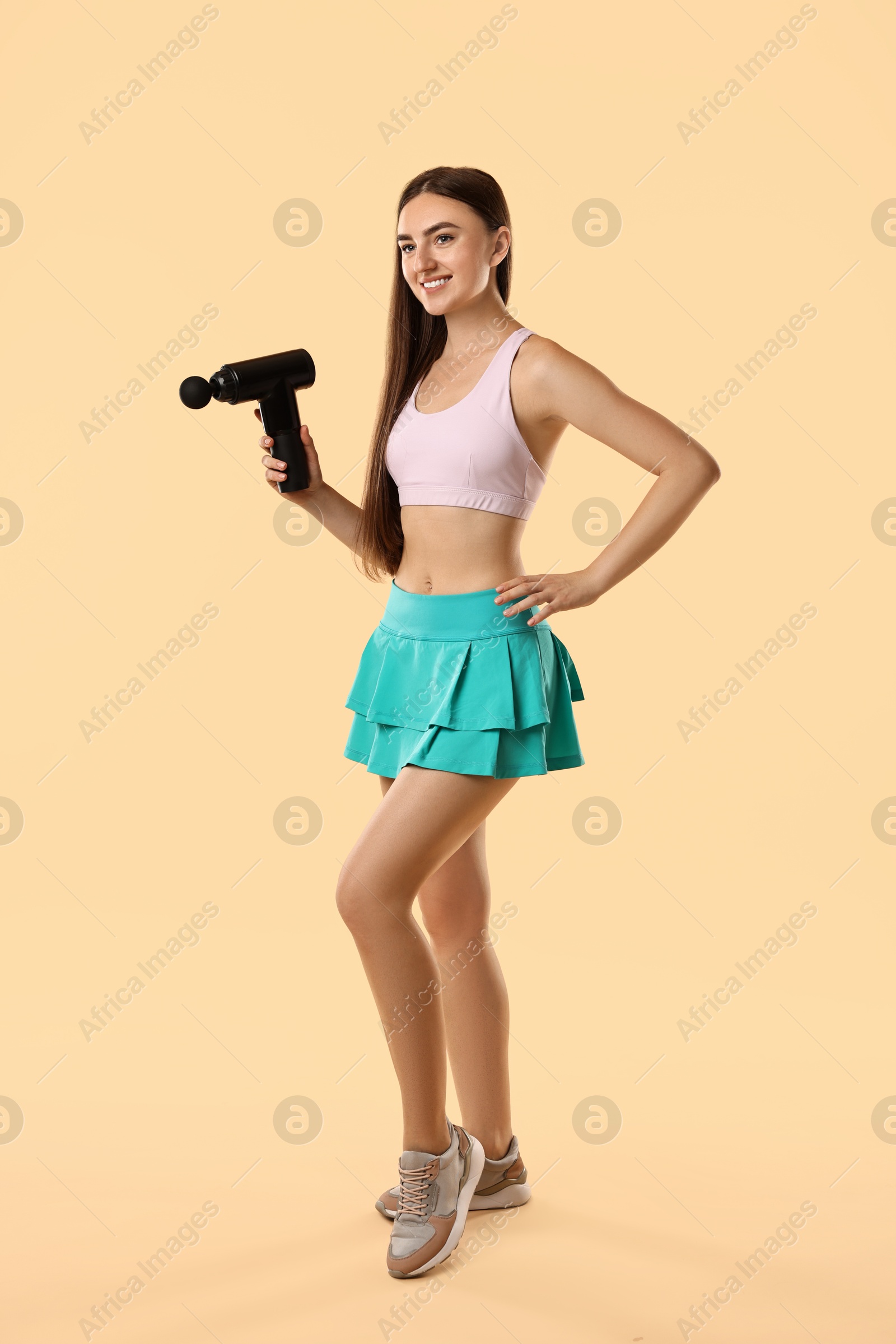 Photo of Young woman with percussive massager on beige background