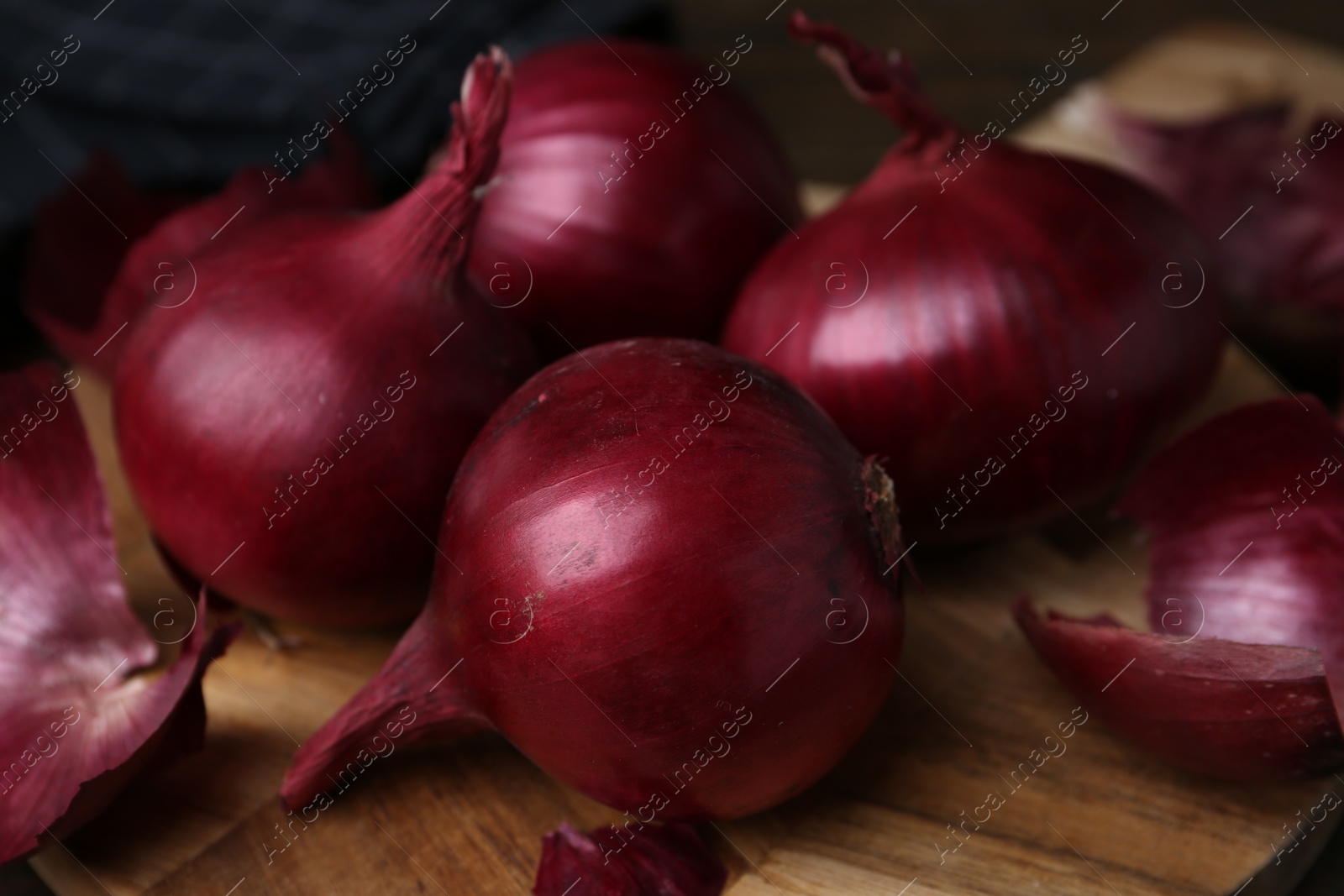 Photo of Fresh onions with peels on wooden board, closeup