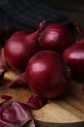 Photo of Fresh onions with peels on wooden board, closeup