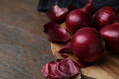 Photo of Fresh onions with peels on wooden table, closeup. Space for text