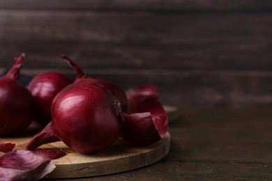 Photo of Fresh onions with peels on wooden table, closeup. Space for text