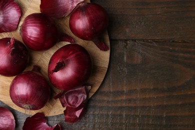 Photo of Fresh onions with peels on wooden table, flat lay. Space for text