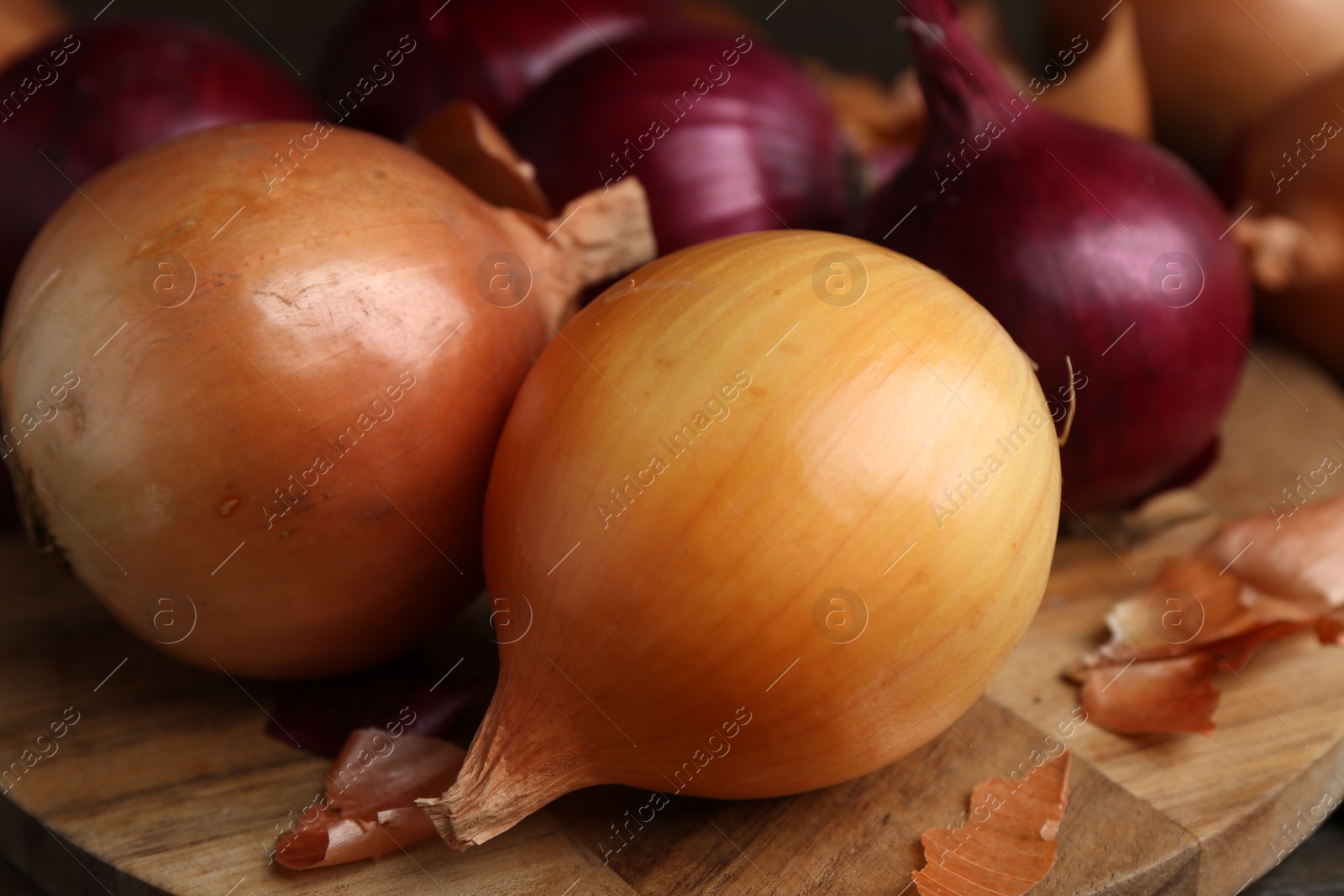 Photo of Fresh onions with peels on wooden board, closeup