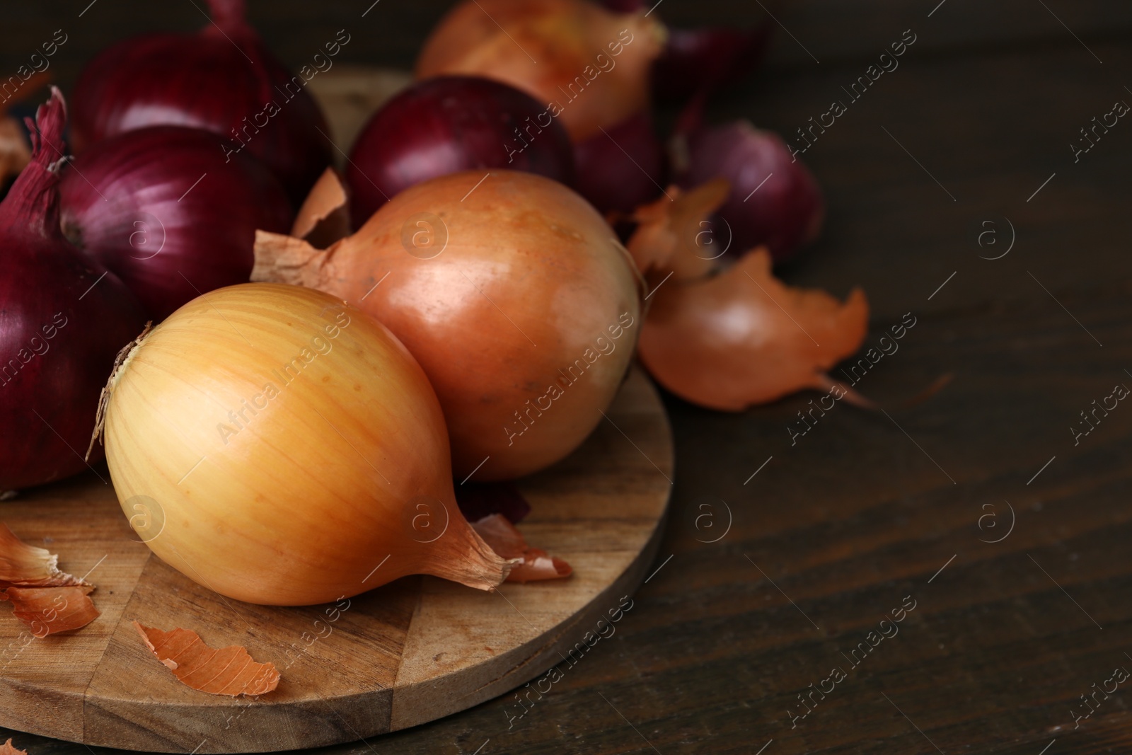 Photo of Fresh onions with peels on wooden table, closeup. Space for text