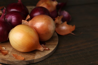 Photo of Fresh onions with peels on wooden table, closeup. Space for text