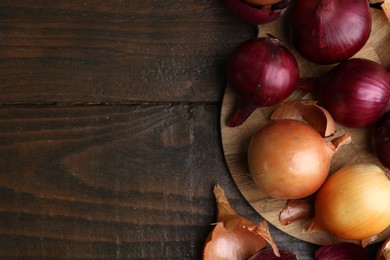 Photo of Fresh onions with peels on wooden table, flat lay. Space for text