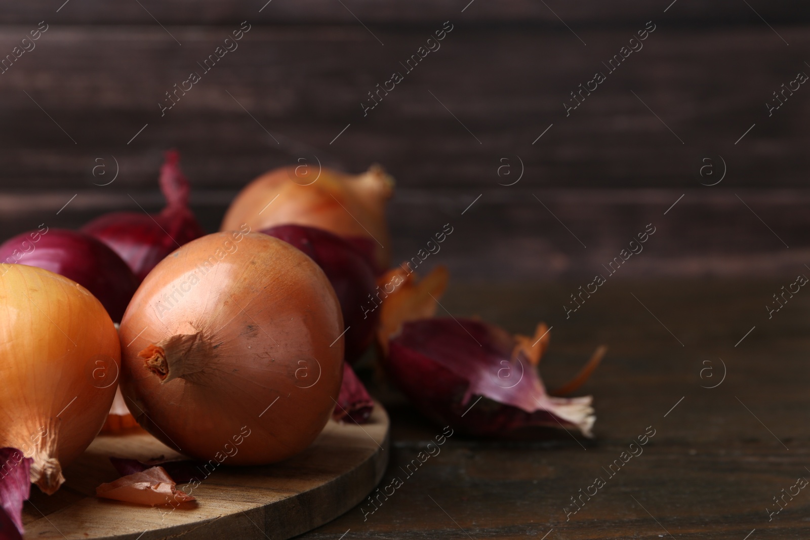 Photo of Fresh onions with peels on wooden table, closeup. Space for text