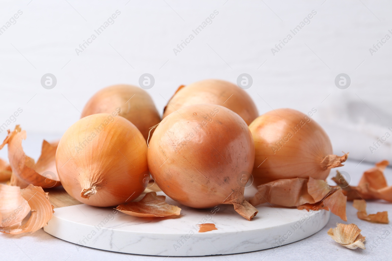 Photo of Fresh onions with peels on light table, closeup