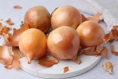 Photo of Fresh onions with peels on light table, closeup