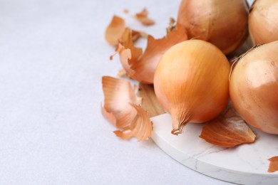 Photo of Fresh onions with peels on light table, closeup. Space for text