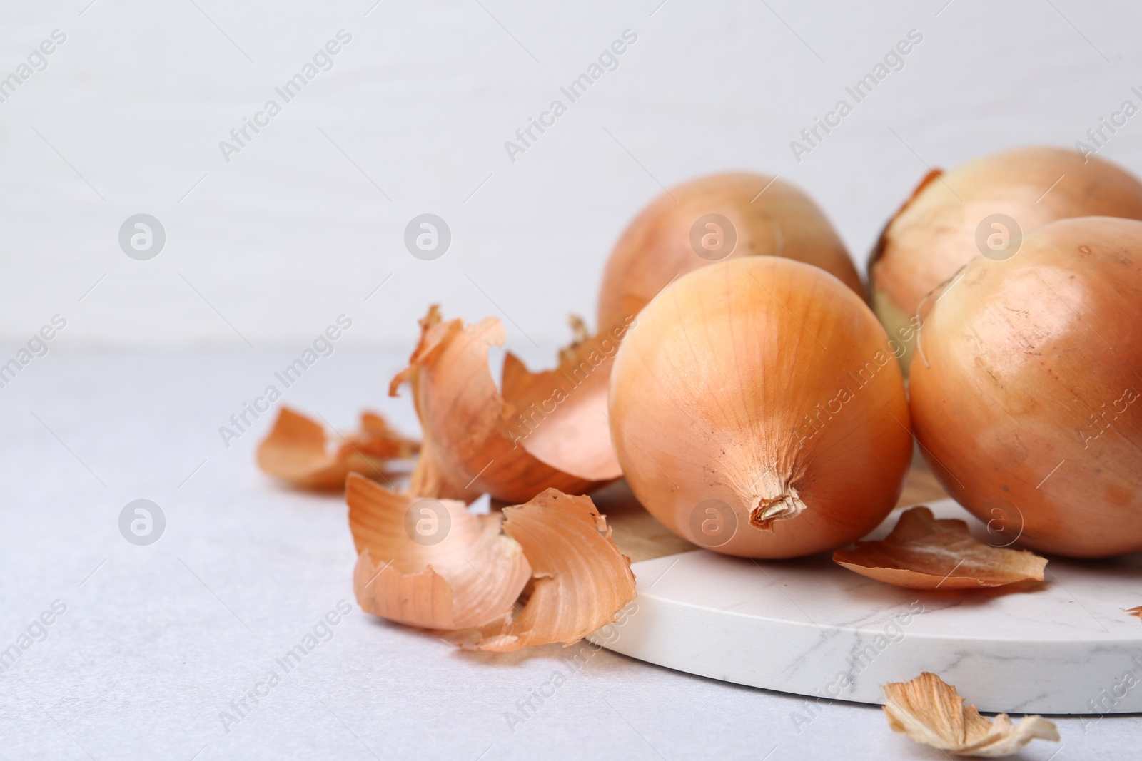 Photo of Fresh onions with peels on light table, closeup. Space for text