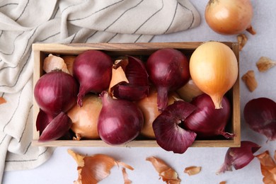 Photo of Crate with fresh onions and peels on light table, flat lay