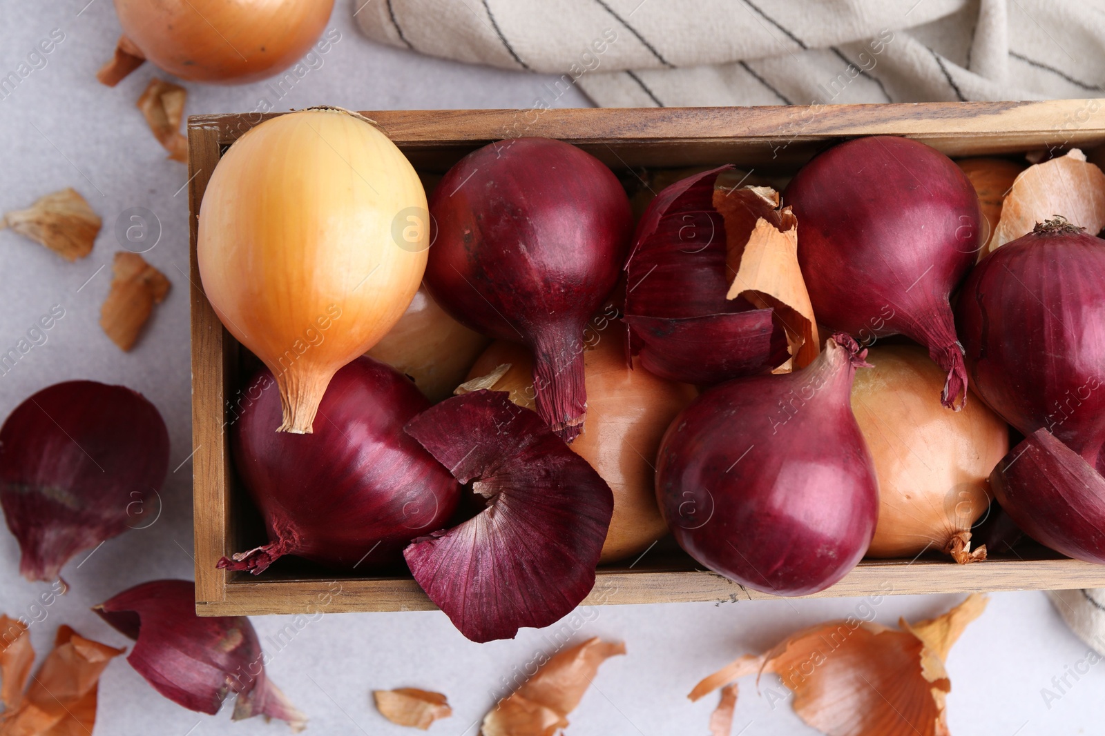 Photo of Crate with fresh onions and peels on light table, flat lay