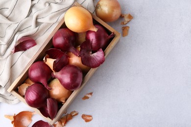 Photo of Crate with fresh onions and peels on light table, flat lay. Space for text