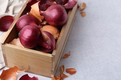 Photo of Crate with fresh onions and peels on light table, closeup. Space for text