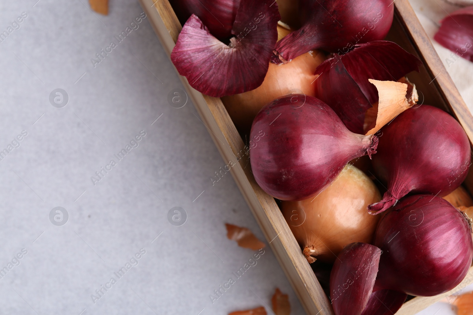 Photo of Crate with fresh onions and peels on light table, top view. Space for text