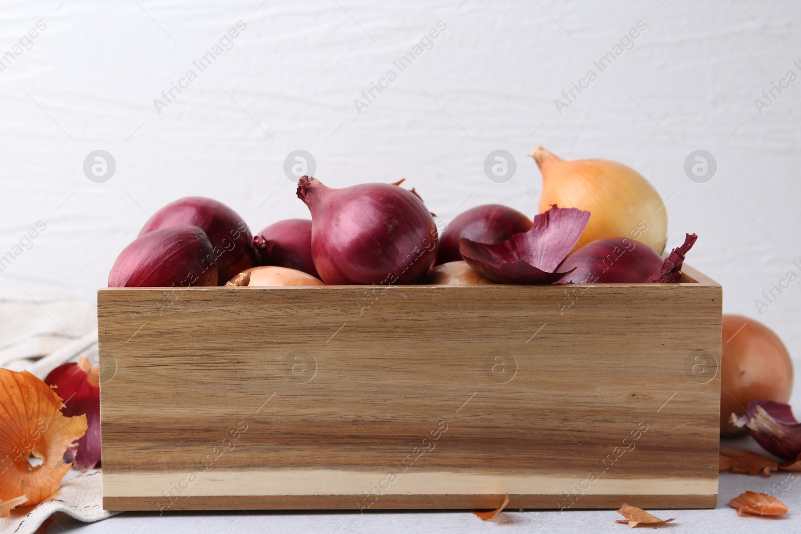 Photo of Crate with fresh onions and peels on light table, closeup