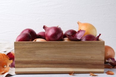 Photo of Crate with fresh onions and peels on light table, closeup