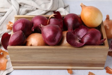 Photo of Crate with fresh onions and peels on light table, closeup