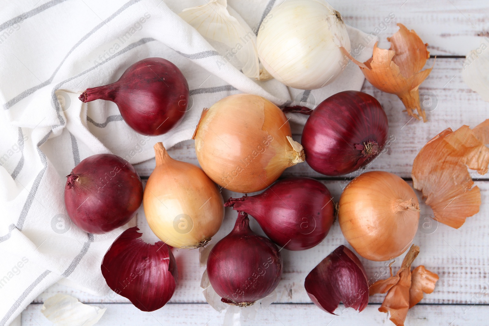 Photo of Fresh onions and peels on light wooden table, flat lay