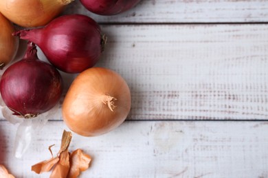 Photo of Fresh onions and peels on light wooden table, flat lay. Space for text