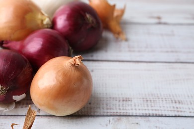 Photo of Fresh onions and peels on light wooden table, closeup. Space for text