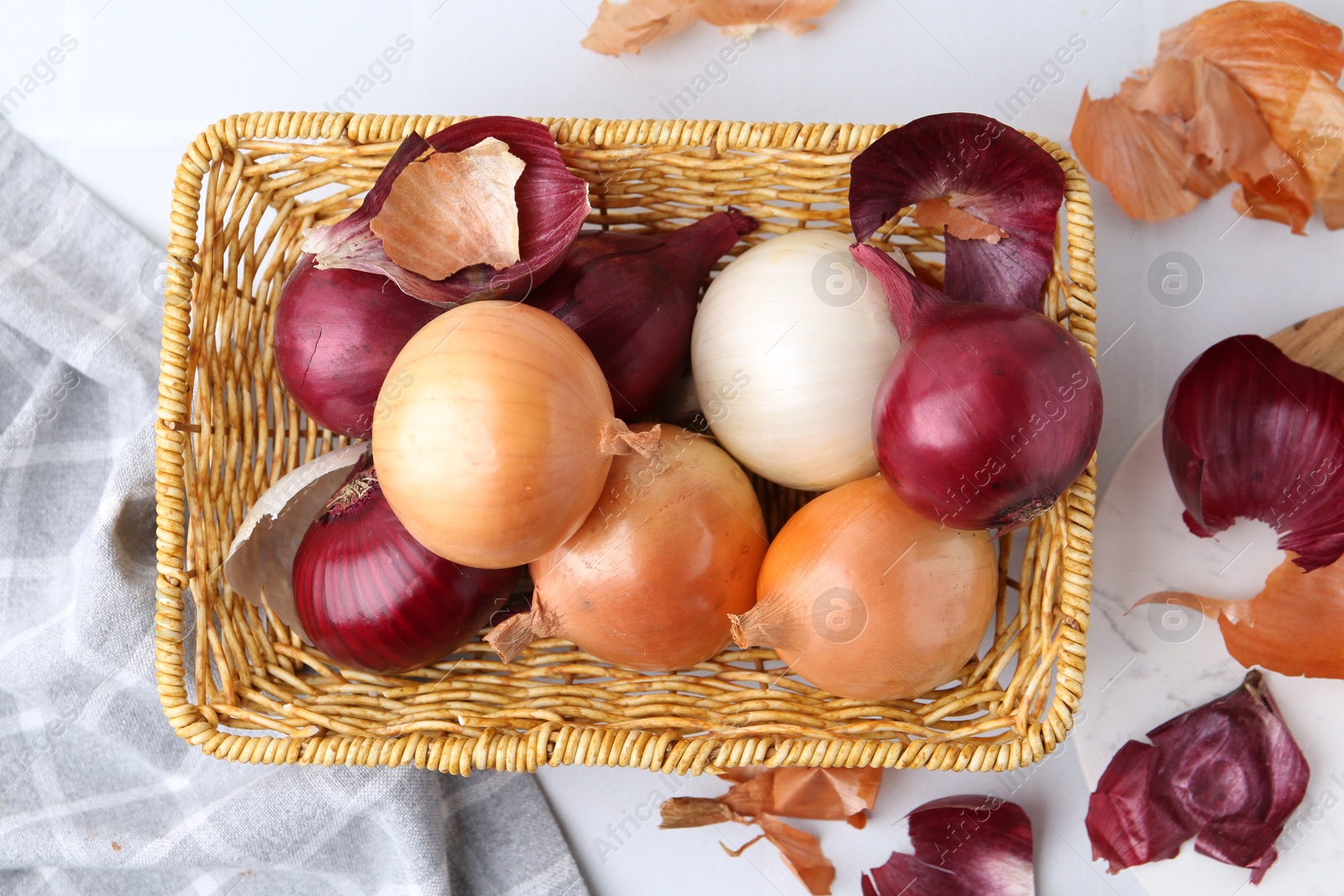 Photo of Wicker basket with fresh onions and peels on light table, flat lay