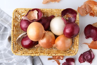 Photo of Wicker basket with fresh onions and peels on light table, flat lay