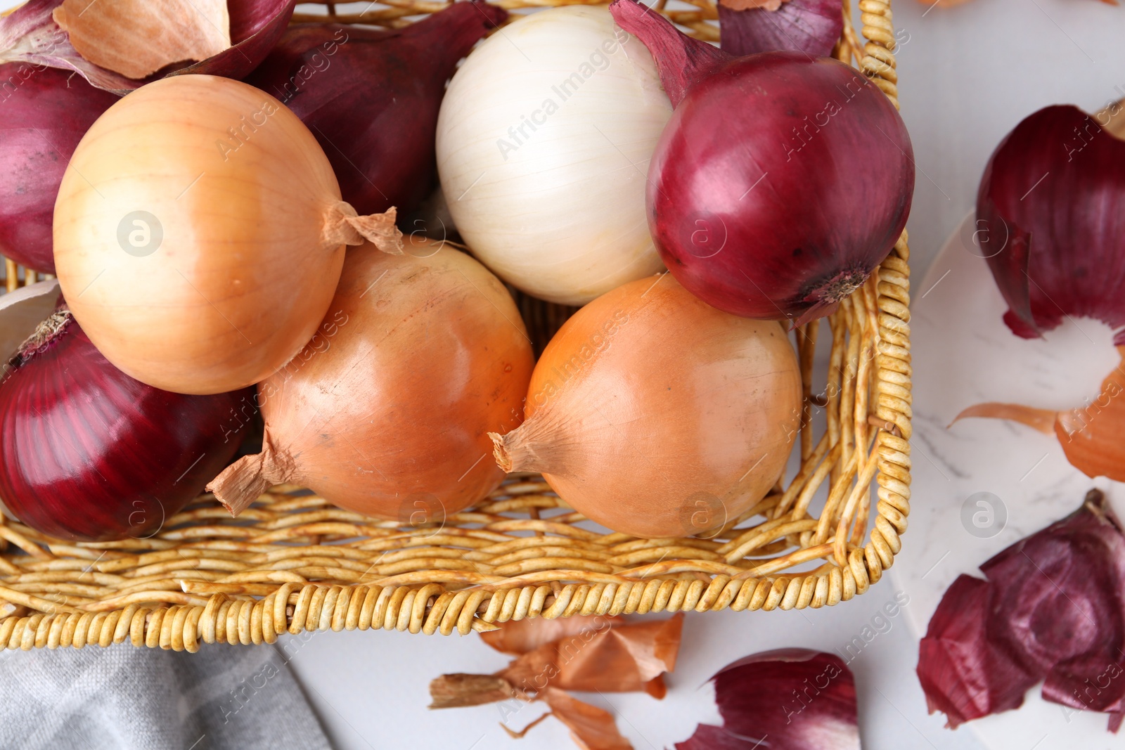 Photo of Wicker basket with fresh onions and peels on light table, flat lay