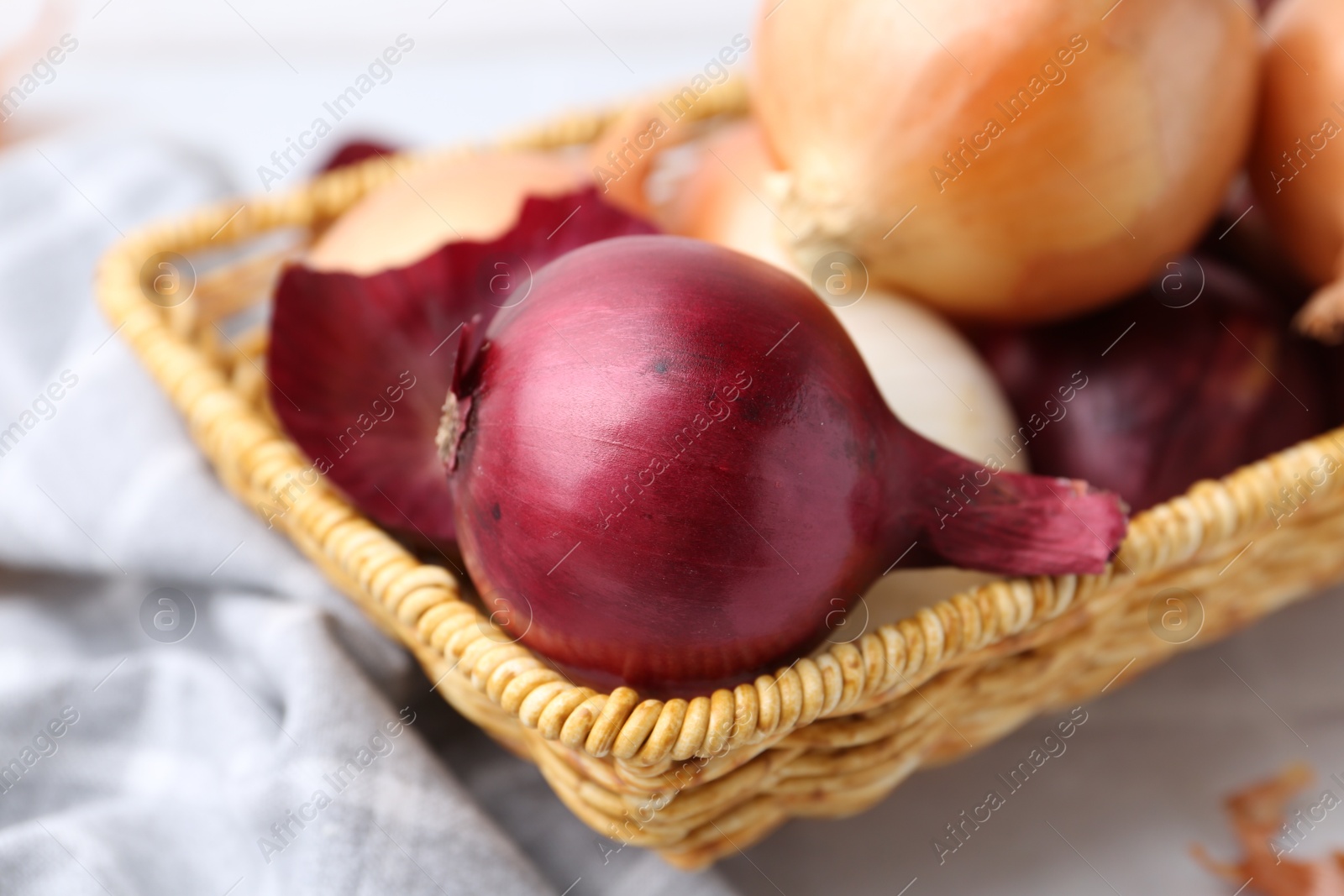 Photo of Wicker basket with fresh onions and peels on white table, closeup