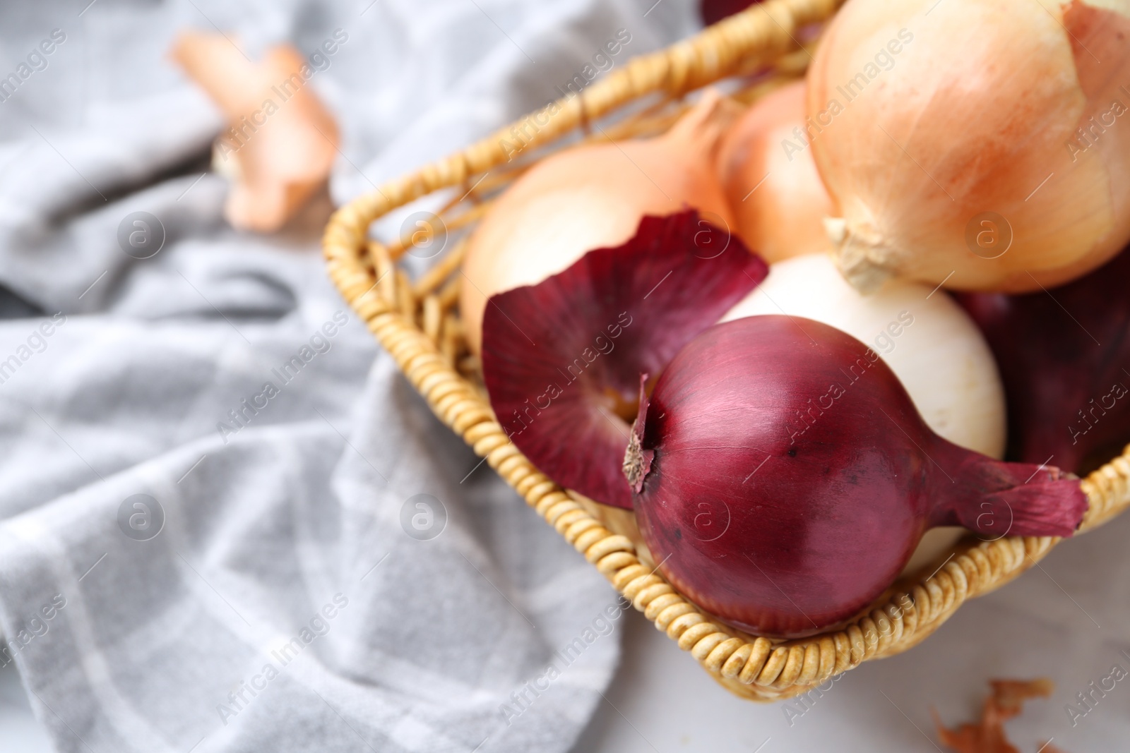 Photo of Wicker basket with fresh onions and peels on white table, closeup. Space for text