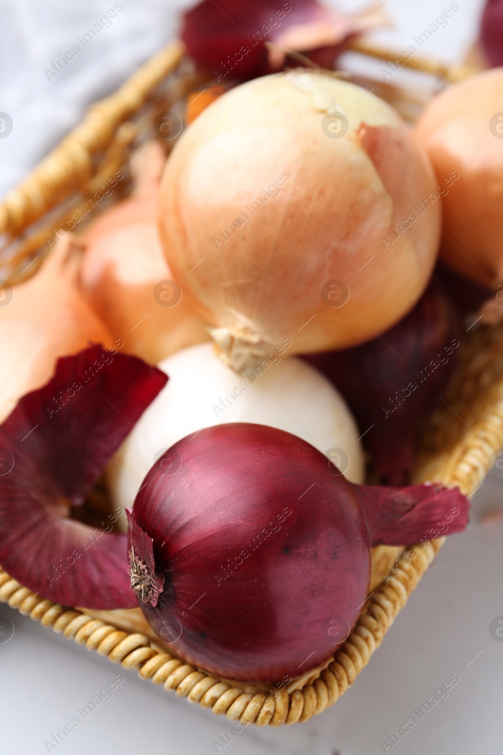 Photo of Wicker basket with fresh onions and peels on white table, closeup