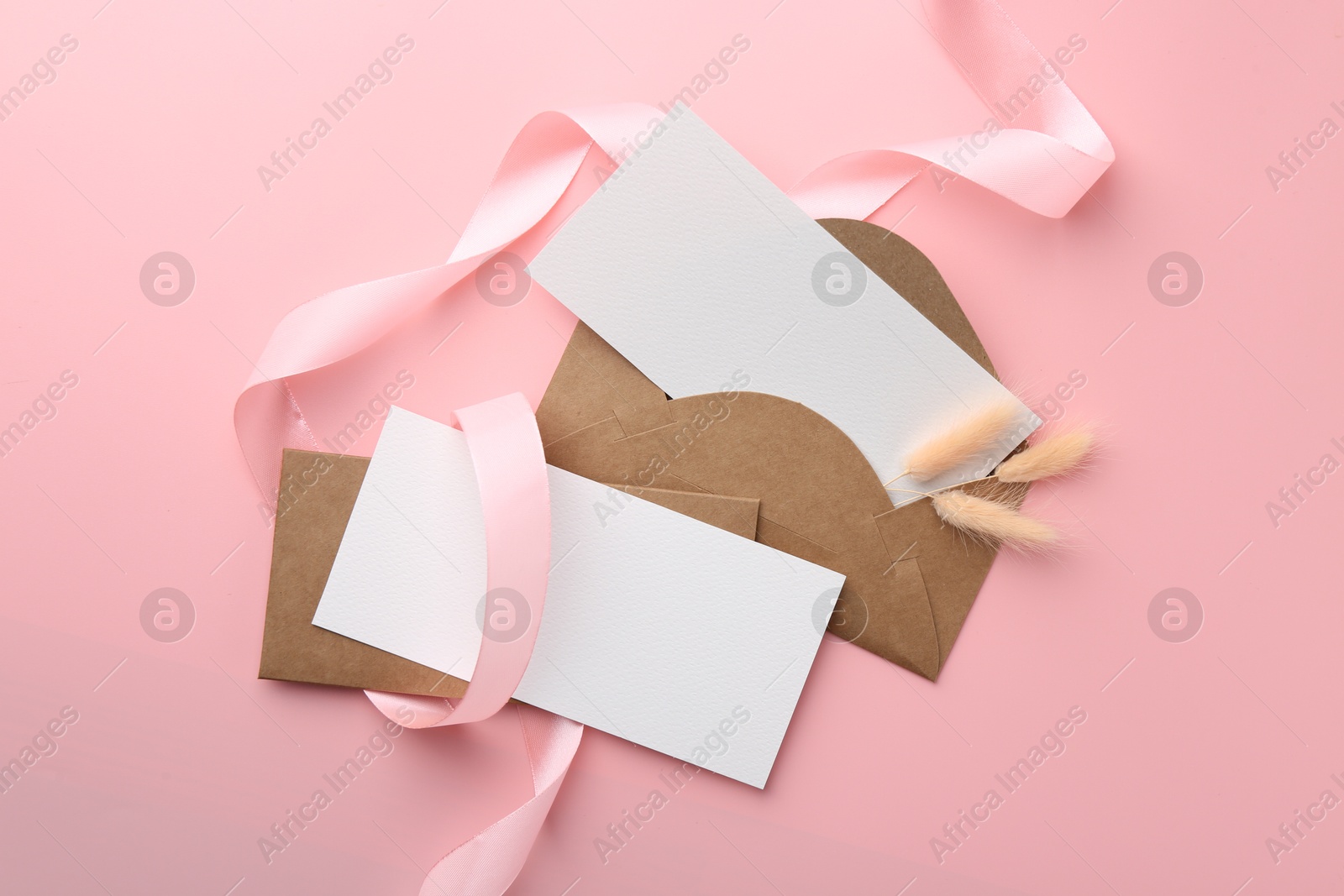 Photo of Blank cards, envelopes, ribbon and spikelets on pink background, flat lay