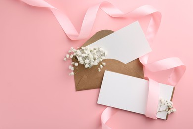 Blank cards, envelopes, ribbon and gypsophila flowers on pink background, flat lay. Space for text