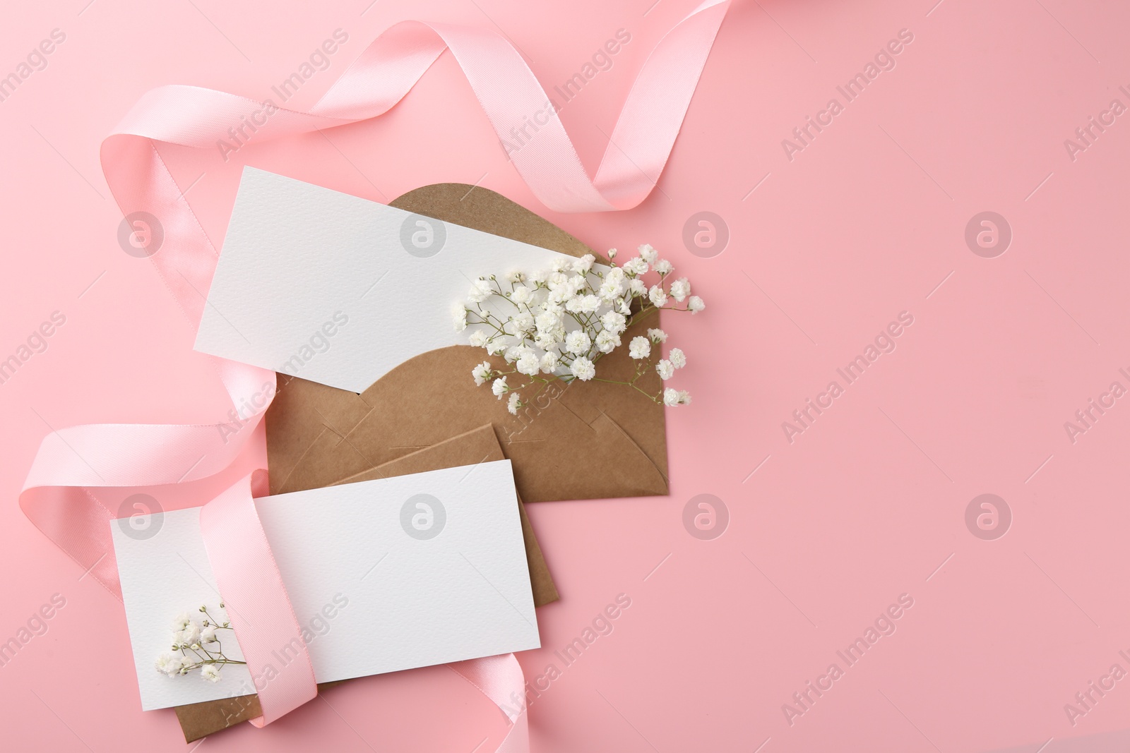 Photo of Blank cards, envelopes, ribbon and gypsophila flowers on pink background, flat lay. Space for text